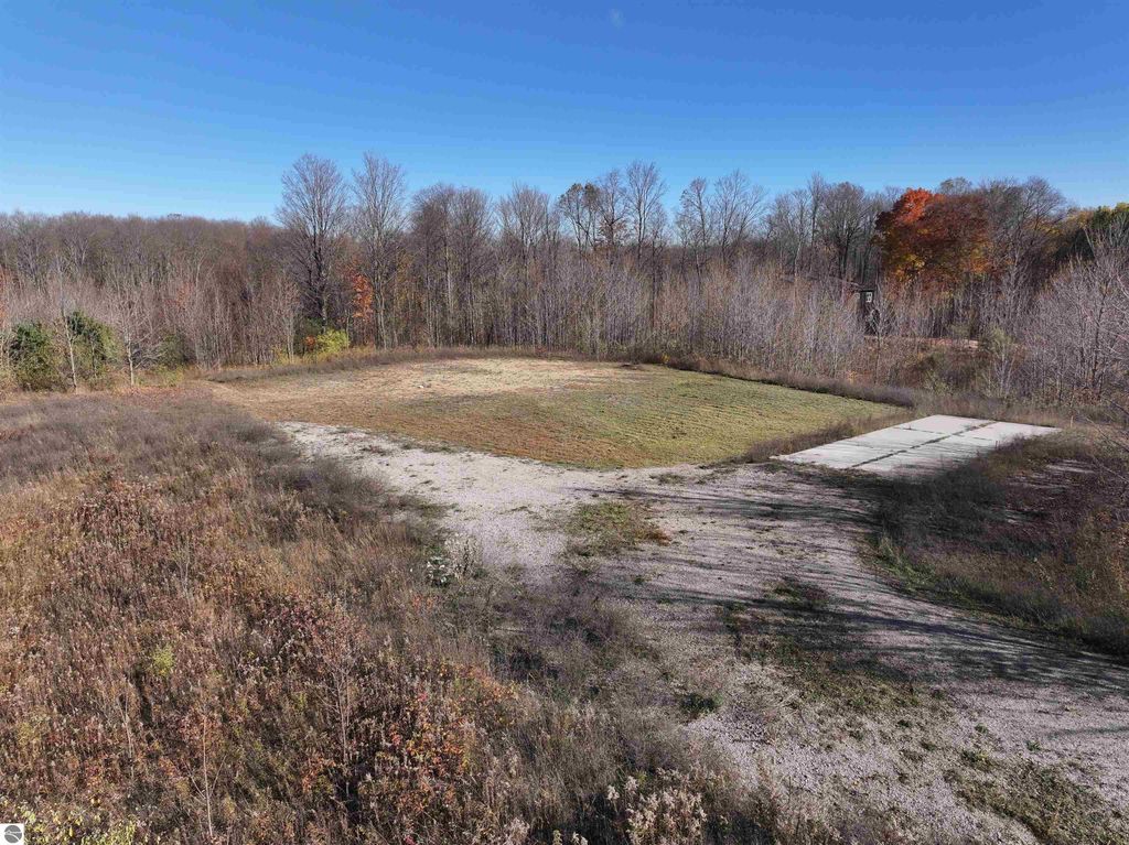Wooded 8-acre parcel in Buckley, MI, featuring a cleared area for building, concrete pad for parking, and surrounding natural landscape.