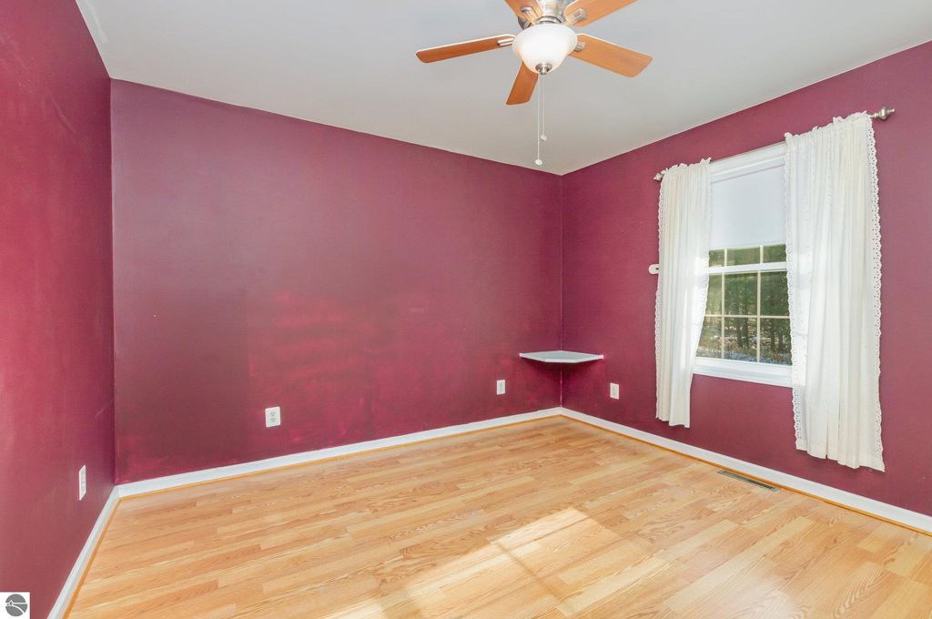 Spacious bedroom with maroon walls, hardwood flooring, ceiling fan, and window with curtains, part of a 4-bedroom home at 650 Linda Drive, Harrison, MI, ideal for a year-round residence or seasonal retreat.
