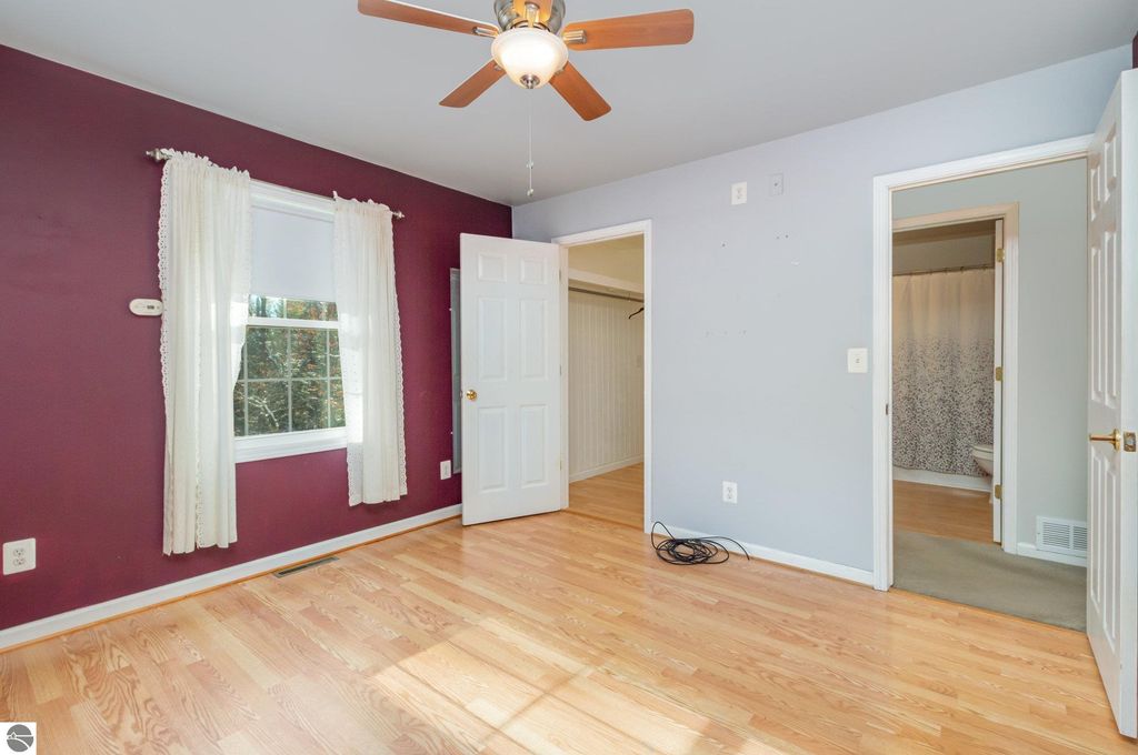 Spacious bedroom with purple accent wall, hardwood floor, window with sheer curtains, and adjoining bathroom entrance in a home for sale at 650 Linda Drive, Harrison, MI.
