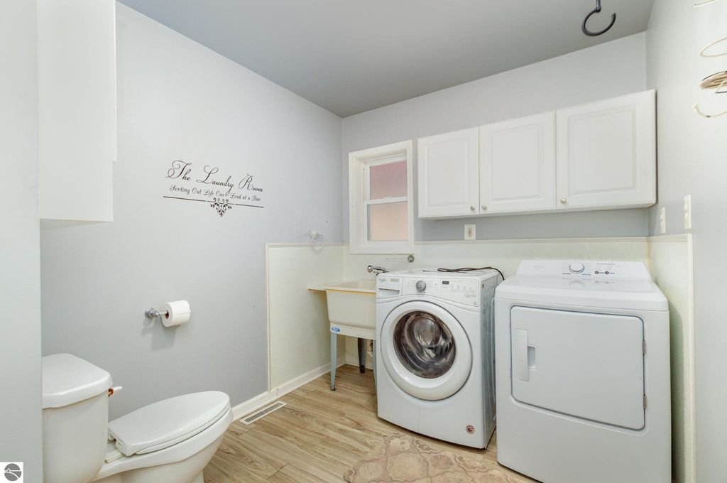 Laundry room featuring a washing machine and dryer, light gray walls, white cabinetry, and a decorative sign reading "The Laundry Room."