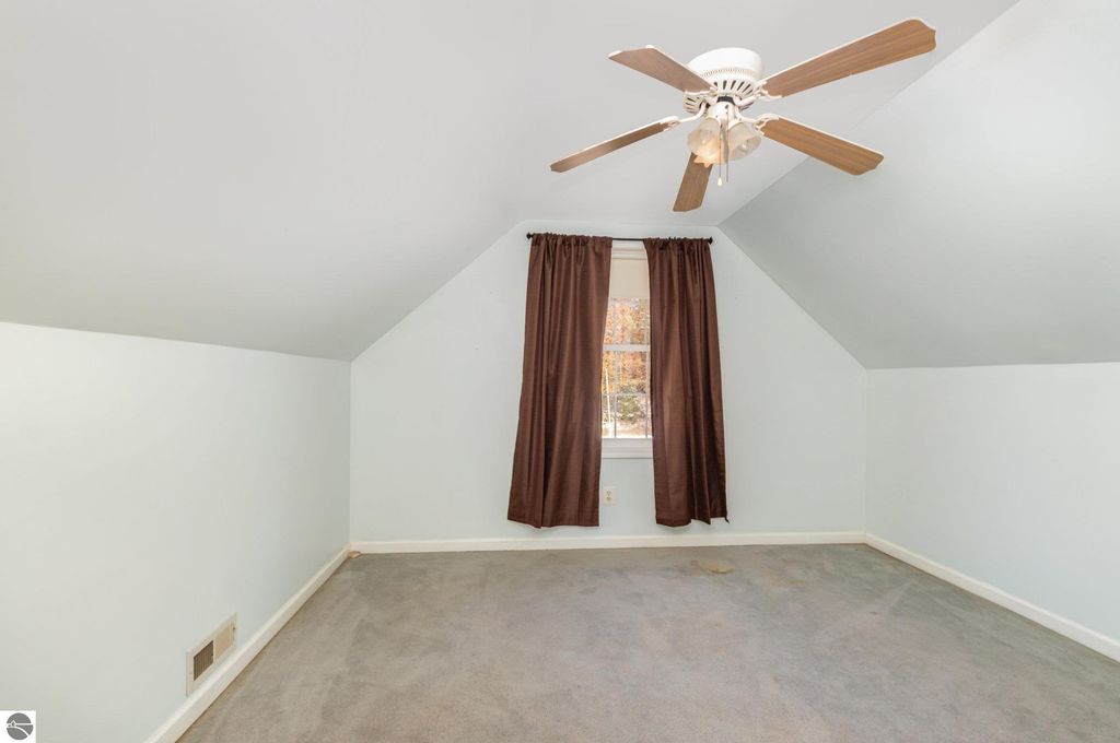 Spacious bedroom in a home at 650 Linda Drive, featuring sloped ceiling, ceiling fan, and large window with brown curtains, showcasing natural light and cozy atmosphere.