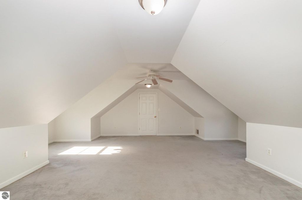 Spacious bonus room above the garage with sloped ceilings, carpeted flooring, and a ceiling fan, ideal for guests or hobbies in a Harrison, MI home.