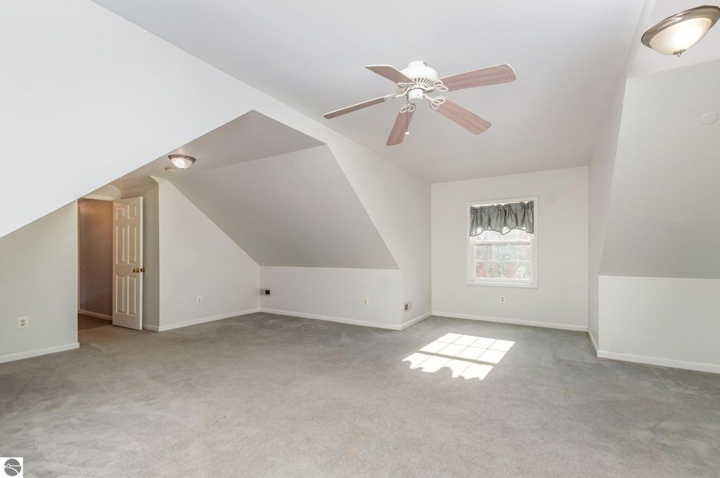Spacious bonus room above the garage in a Harrison, MI home, featuring sloped ceilings, a ceiling fan, and natural light from a window, ideal for guests or hobbies.