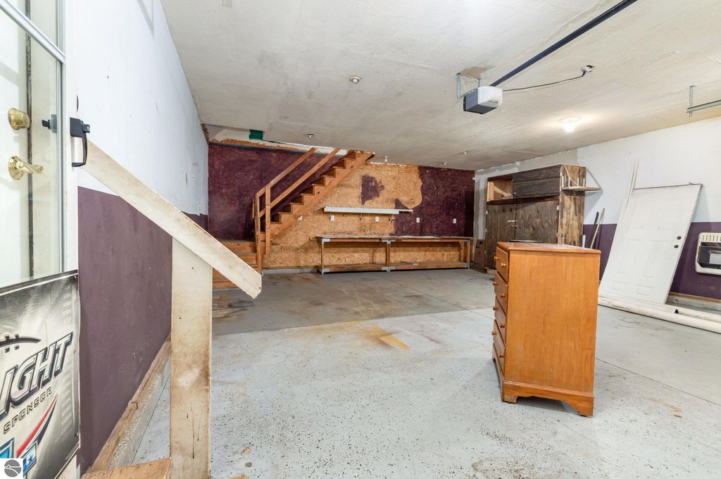 Spacious interior of a garage featuring wooden shelving, a staircase, and a dresser, highlighting storage potential for recreational equipment and vehicles at 650 Linda Drive, Harrison, MI.