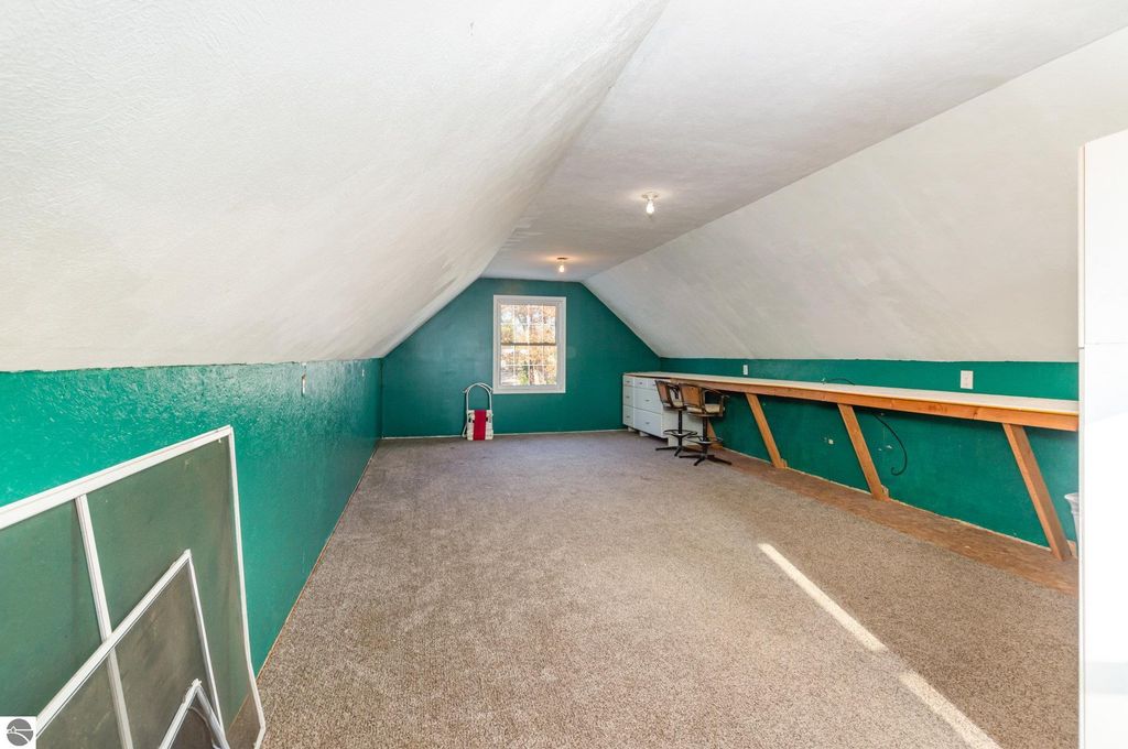 Spacious bonus room above garage with green walls, carpeted floor, and large window, offering flexible space for guests or hobbies in Harrison, MI home for sale.