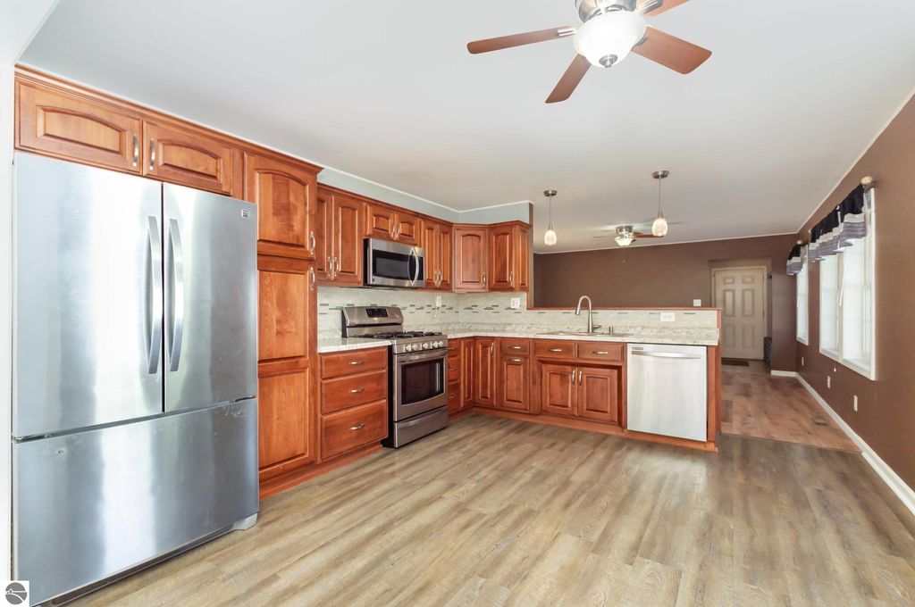 Modern kitchen with stainless steel appliances, including a refrigerator and oven, wooden cabinetry, and a spacious layout, highlighting the home at 650 Linda Drive, Harrison, MI.