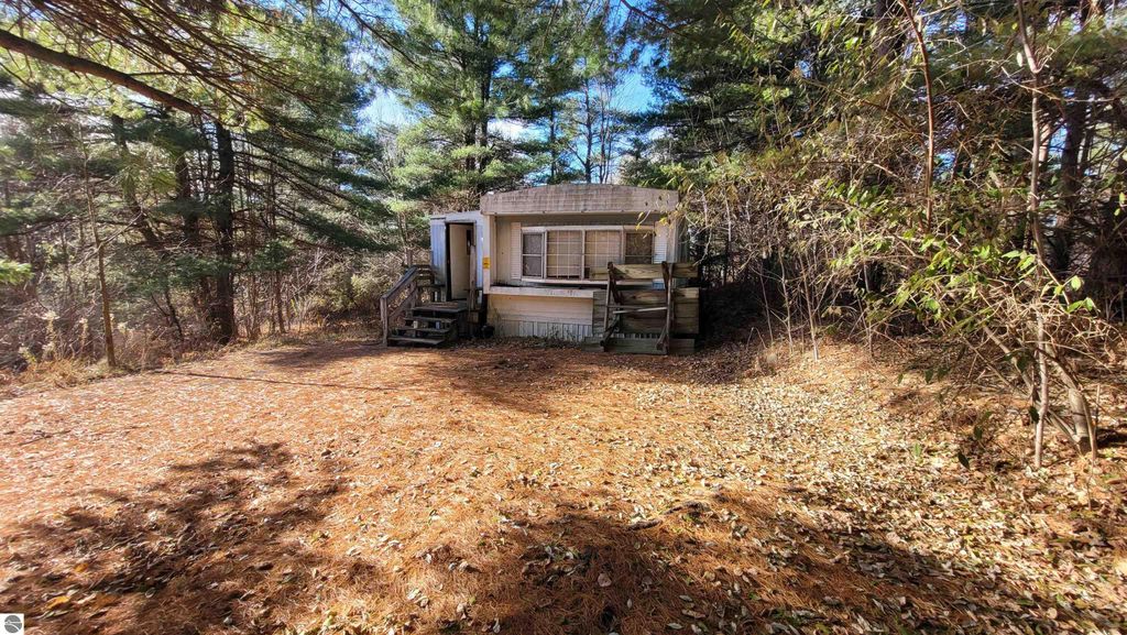 Mobile home on 40 acres in Alden, MI, surrounded by trees and rolling topography, showcasing potential for development and outdoor activities.