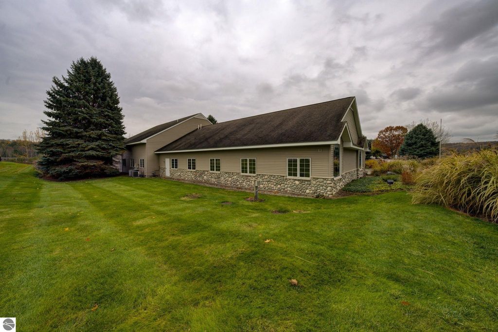Exterior view of commercial property at 7200 E Duck Lake Road, Lake Leelanau, featuring landscaped lawn, stone foundation, and large windows, surrounded by trees and open space.