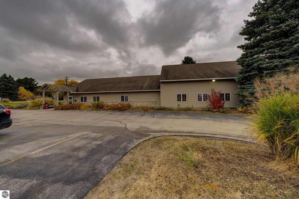 Commercial building exterior at 7200 E Duck Lake Road, Lake Leelanau, MI, featuring a parking area, landscaping, and cloudy sky, highlighting investment opportunity in a growing community.