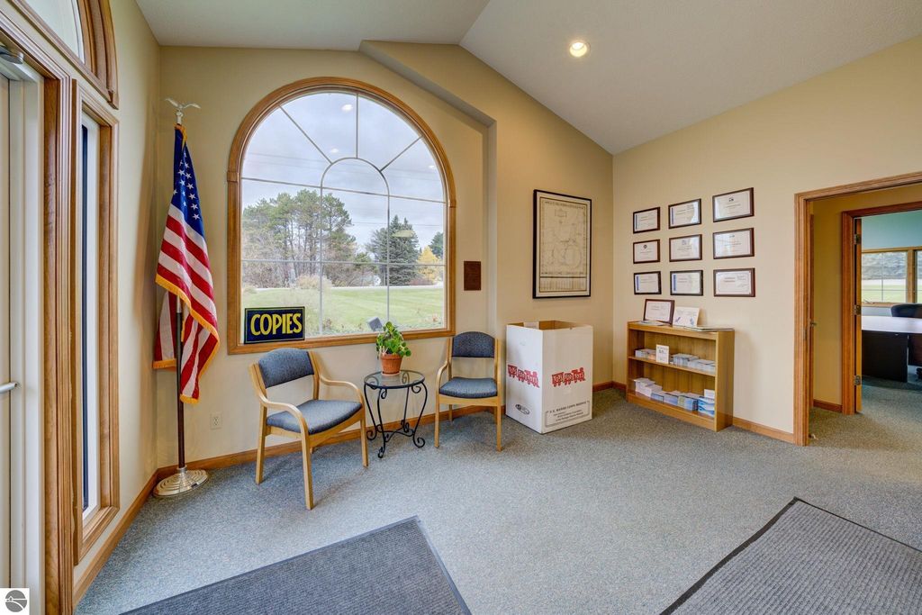 Reception area of a commercial building featuring an American flag, a "COPIES" sign, two chairs, a small table with a plant, and various certificates displayed on the wall, highlighting the professional environment of the property at 7200 E Duck Lake Road, Lake Leelanau, MI.
