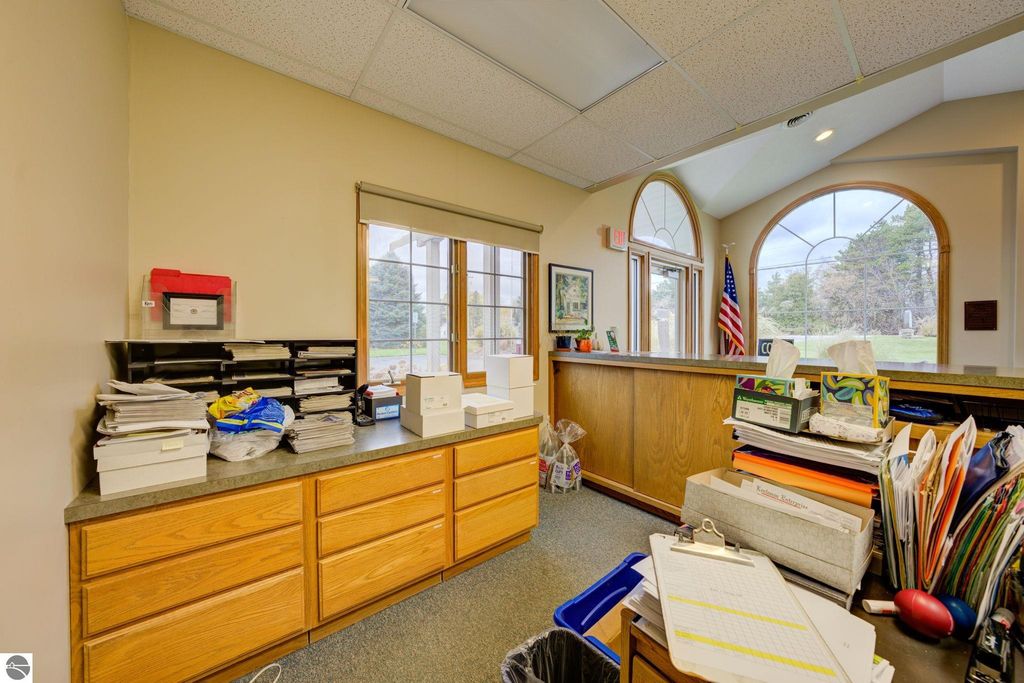 Reception area with wooden counter, cluttered with papers and office supplies, large windows allowing natural light, American flag visible, and artwork on the walls, indicative of a commercial office space in Lake Leelanau.