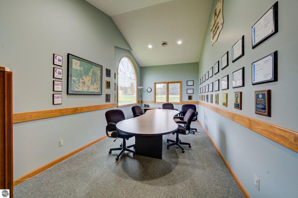 Conference room with a round table, office chairs, wall-mounted awards, and a large window, showcasing a professional workspace in a commercial building for sale in Lake Leelanau, MI.