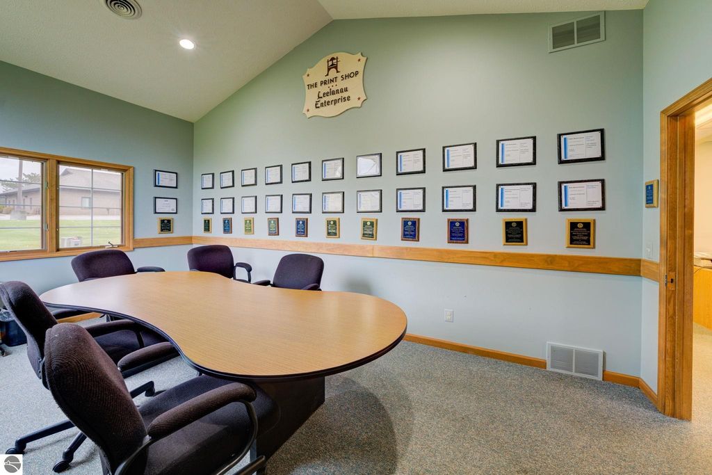 Conference room featuring a large round table, black chairs, and a wall adorned with various awards and certificates, highlighting the Leelanau Enterprise's achievements in a commercial space at 7200 E Duck Lake Road, Lake Leelanau, MI.