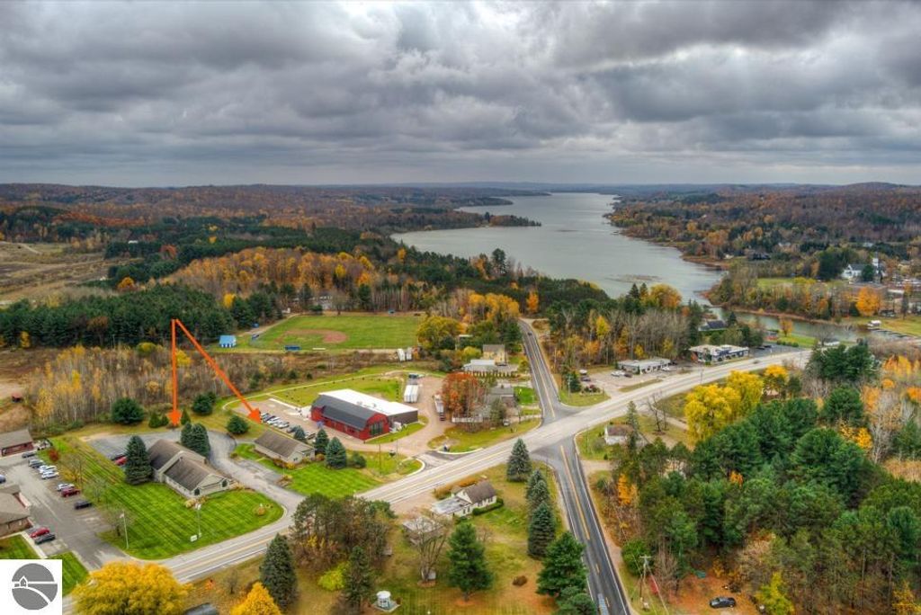Aerial view of commercial property at 7200 E Duck Lake Road, Lake Leelanau, showcasing two buildings, green lawns, and surrounding landscape with autumn foliage and nearby water body.