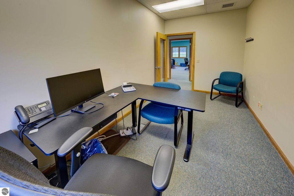 Office interior featuring a desk with a computer monitor, office phone, and two blue chairs, showcasing a professional workspace in a commercial building for lease in Lake Leelanau.