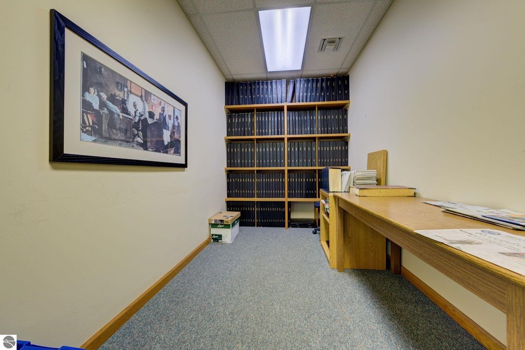 Office interior featuring a framed artwork, shelves filled with binders, and a wooden desk, reflecting a professional workspace in a commercial property for sale in Lake Leelanau.