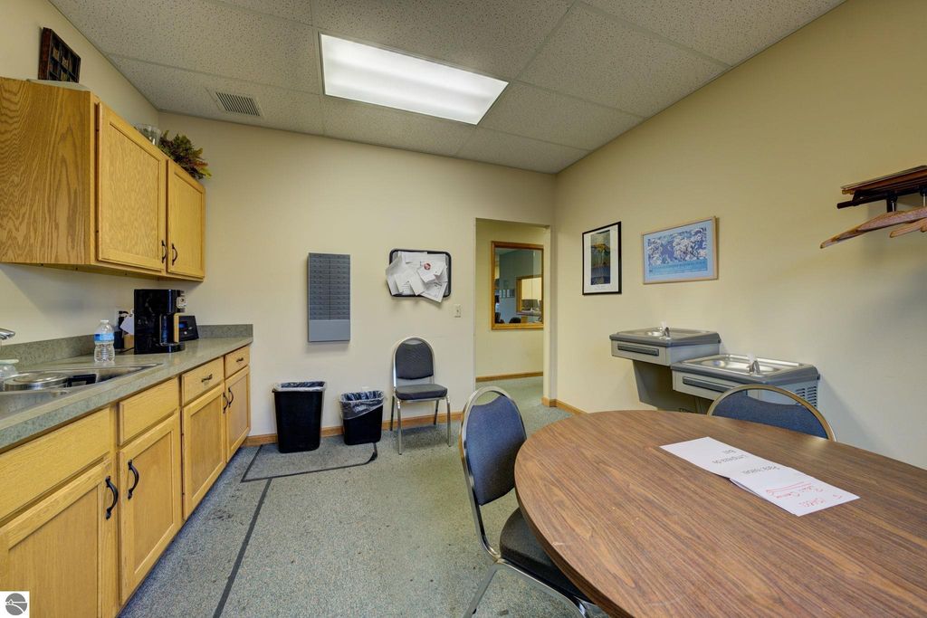 Kitchen area with wooden cabinets, round table, and water cooler in commercial property at 7200 E Duck Lake Road, Lake Leelanau, MI.
