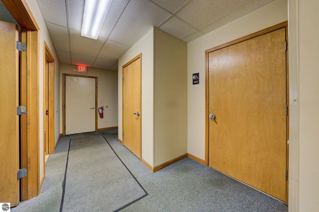 Hallway interior featuring multiple wooden doors, exit sign, fire extinguisher, and a women's restroom sign, showcasing the layout of the commercial property at 7200 E Duck Lake Road, Lake Leelanau, MI.