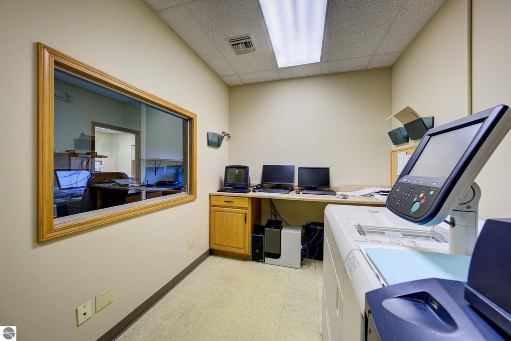 Office space featuring two computers on a desk, a printer, and a window showcasing a work area, relevant to the commercial real estate listing at 7200 E Duck Lake Road, Lake Leelanau, MI.