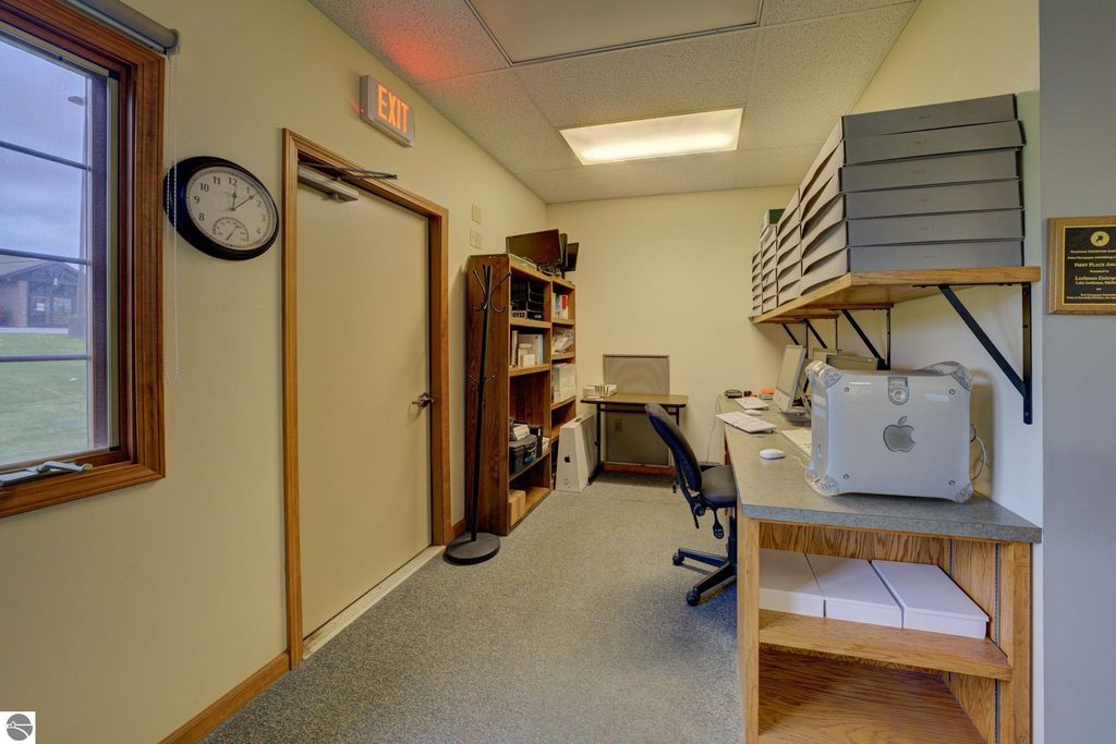 Interior office space featuring a desk with a computer, shelves with storage boxes, a clock, and an exit door, reflecting the functional layout of a commercial building in Lake Leelanau.