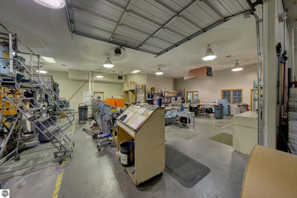 Interior view of a commercial manufacturing space featuring printing machinery, workstations, and storage areas, highlighting the property&rsquo;s potential for future build-out and business operations in Lake Leelanau, MI.