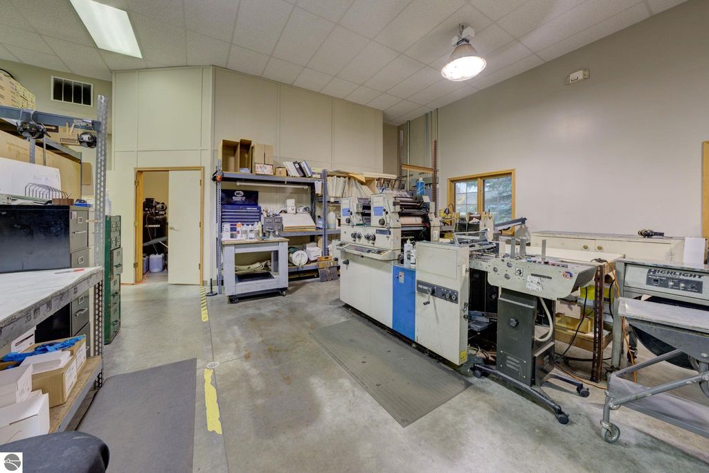 Commercial printing workspace featuring printing machinery, storage shelves, and office supplies, emphasizing the operational potential of the property at 7200 E Duck Lake Road, Lake Leelanau, MI.