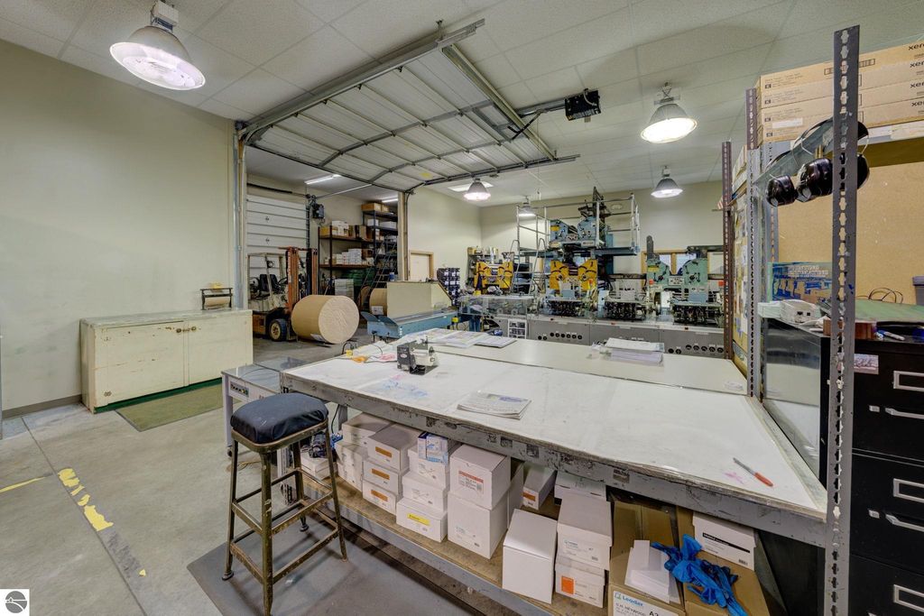 Interior view of commercial workspace featuring a large work table, storage units, printing machinery, and organizational shelves, highlighting the leased production space at 7200 E Duck Lake Road, Lake Leelanau, MI.