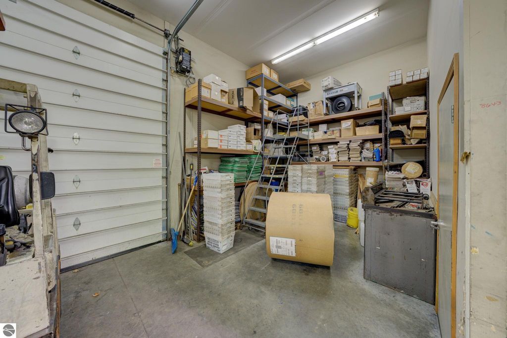 Storage space with shelving units filled with boxes, a rolling ladder, and a garage door, illustrating flexible potential for commercial use at 7200 E Duck Lake Road, Lake Leelanau, MI.