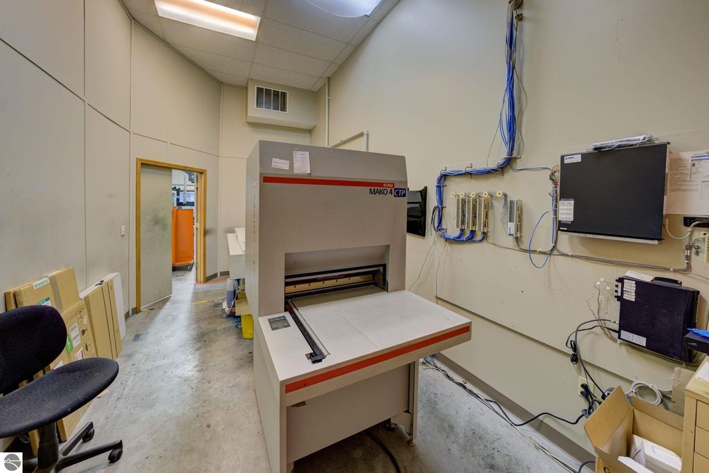 Printing equipment in a commercial building, featuring a Mako 4 CTP machine, surrounded by storage boxes and office furniture, illustrating workspace for a leased printing business at 7200 E Duck Lake Road, Lake Leelanau, MI.