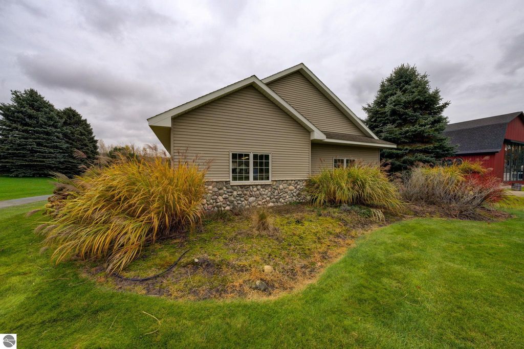 Commercial building exterior at 7200 E Duck Lake Road, Lake Leelanau, MI, featuring landscaped area with ornamental grasses, stone foundation, and nearby trees, highlighting investment potential in a growing community.