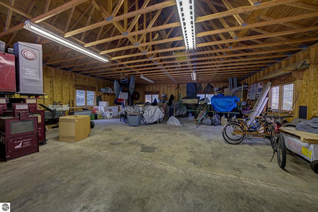 Spacious interior of a commercial storage building in Lake Leelanau, featuring exposed wooden beams, various equipment, bicycles, and covered items, showcasing flexible potential for future use.