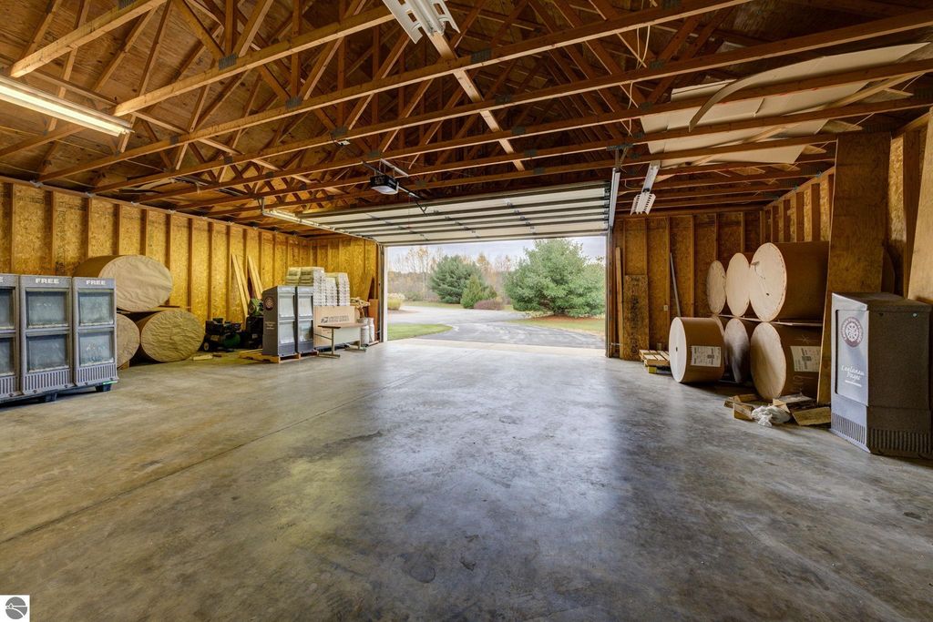 Interior view of a commercial building in Lake Leelanau, featuring storage space with large rolls of material, industrial shelving, and a garage door leading to the exterior, highlighting the flexible potential for future build-out.