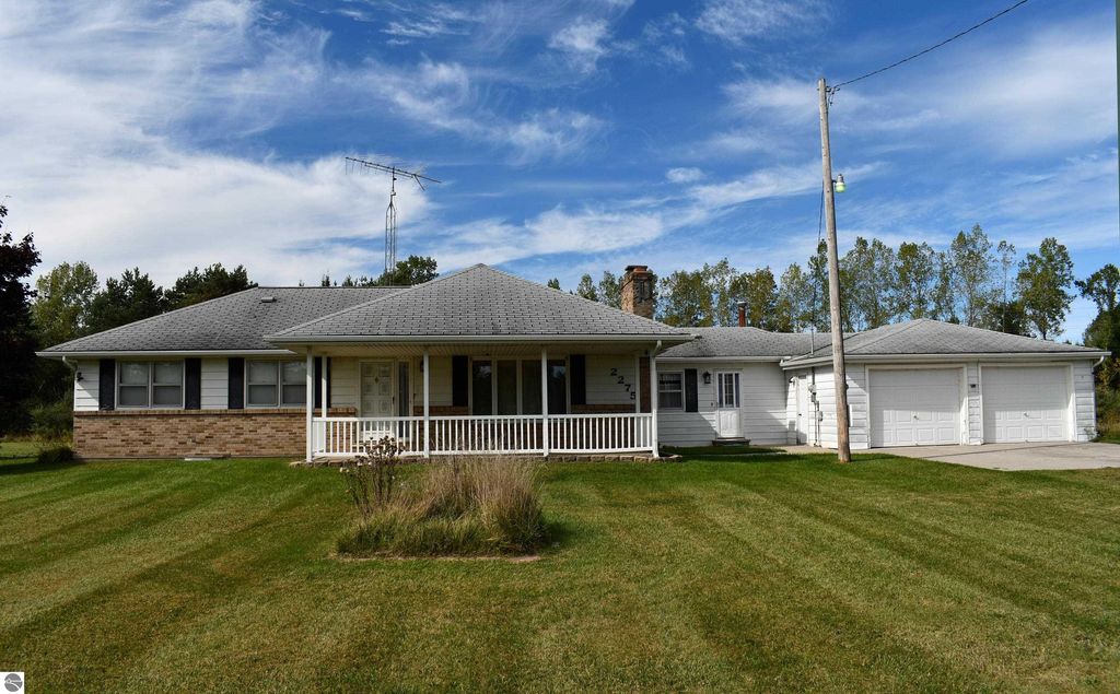 Ranch-style home at 2275 Noble Road, Tawas City, MI, featuring a spacious front porch, manicured lawn, and attached garage, set on 40 acres of private land.