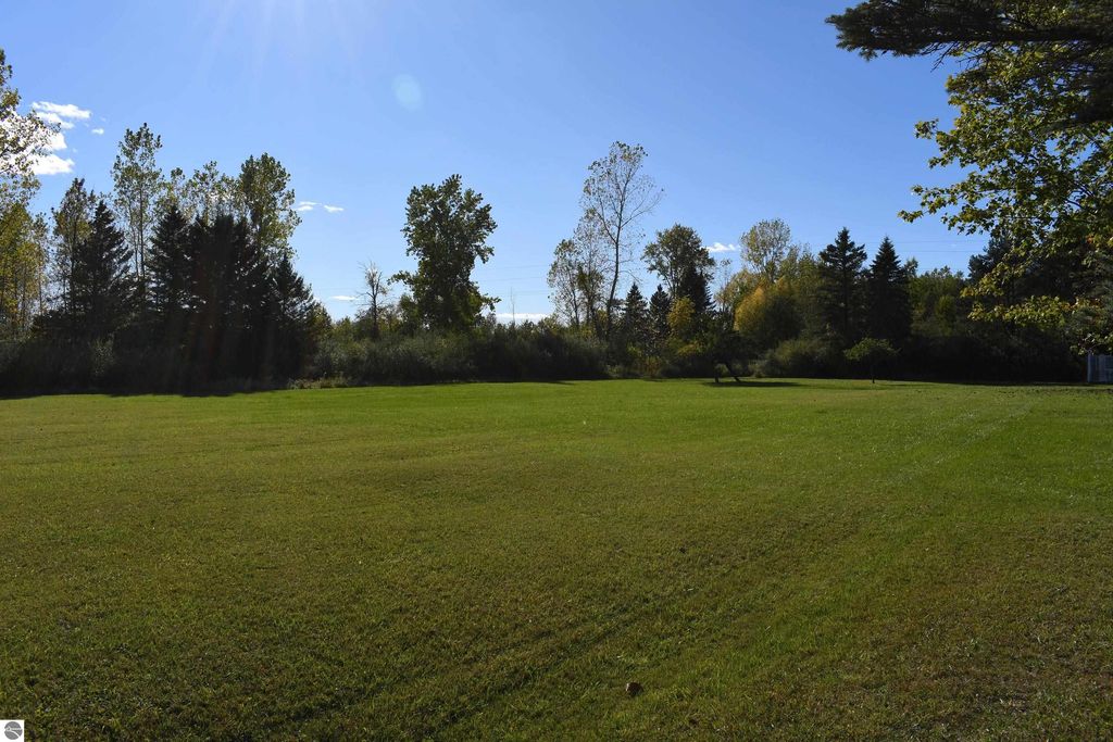 Expansive green lawn with trees and blue sky, showcasing the 40-acre property at 2275 Noble Road, Tawas City, ideal for outdoor activities and privacy.