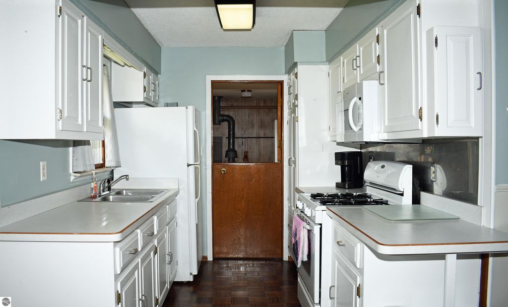 Kitchen interior of a ranch-style home featuring white cabinetry, stainless steel appliances, and a window with natural light, showcasing a functional layout ideal for comfortable living in Tawas City, MI.