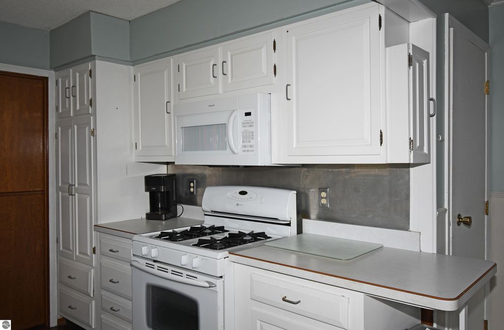 Kitchen interior featuring white cabinetry, gas stove, microwave, and coffee maker, emphasizing a cozy and functional space in the ranch home at 2275 Noble Road, Tawas City, MI.