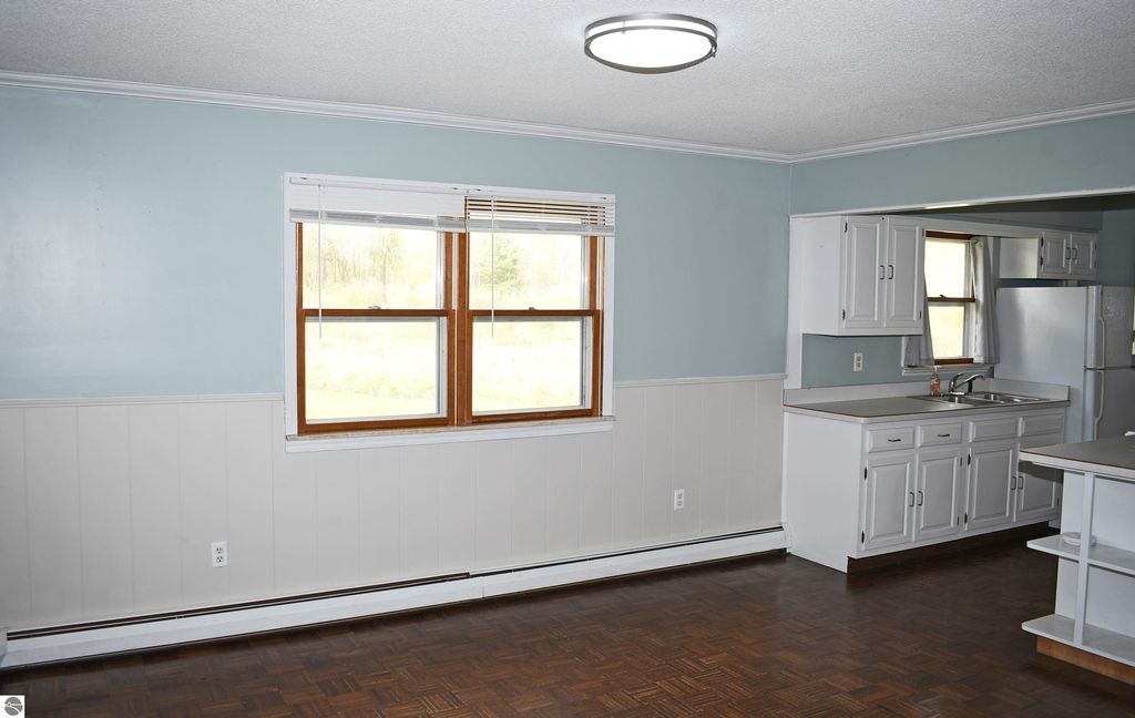 Interior view of a ranch-style home kitchen at 2275 Noble Road, Tawas City, featuring light blue walls, white cabinetry, and a window overlooking the surrounding 40 acres.