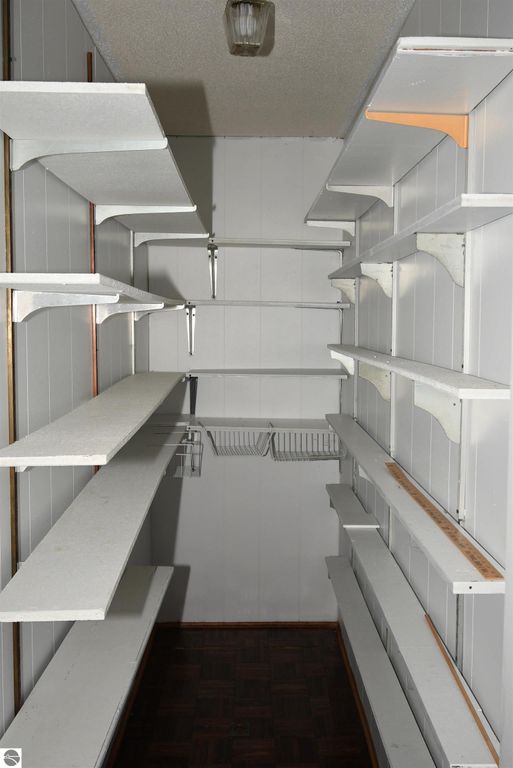 Empty pantry with white shelves and wooden floor, showcasing ample storage space in the ranch-style home at 2275 Noble Road, Tawas City, MI.