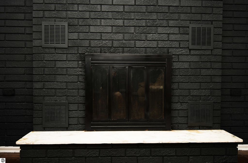 Black brick wall with a natural wood-burning fireplace and marble mantel, showcasing a cozy interior feature for the ranch-style home at 2275 Noble Road, Tawas City, MI.