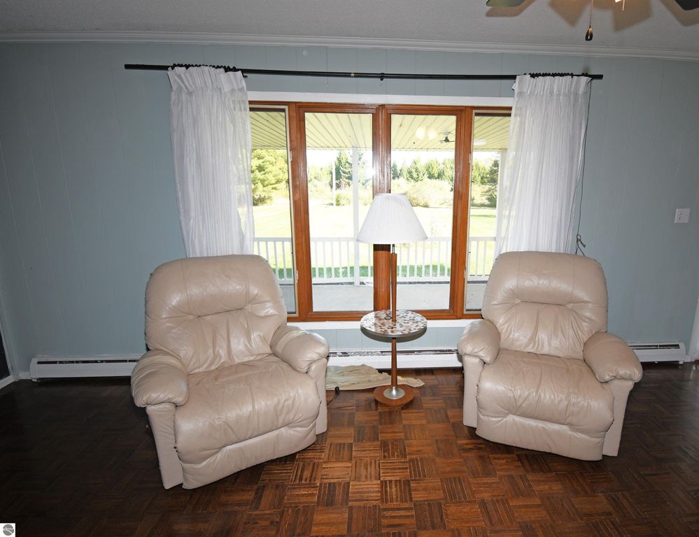 Cozy living room featuring two beige recliners, a side table with a lamp, and large windows showcasing the serene outdoor view of the 40-acre property in Tawas City, MI.