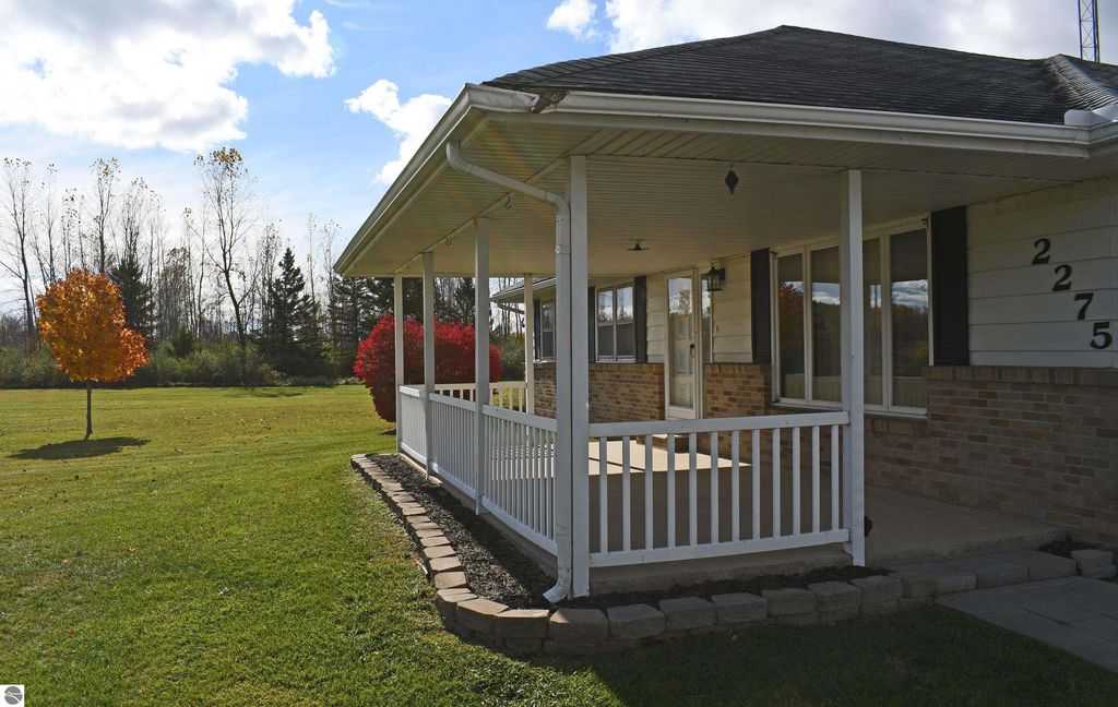 Ranch-style home exterior at 2275 Noble Road in Tawas City, featuring a covered porch, landscaped yard with colorful trees, and a serene rural setting on 40 acres.
