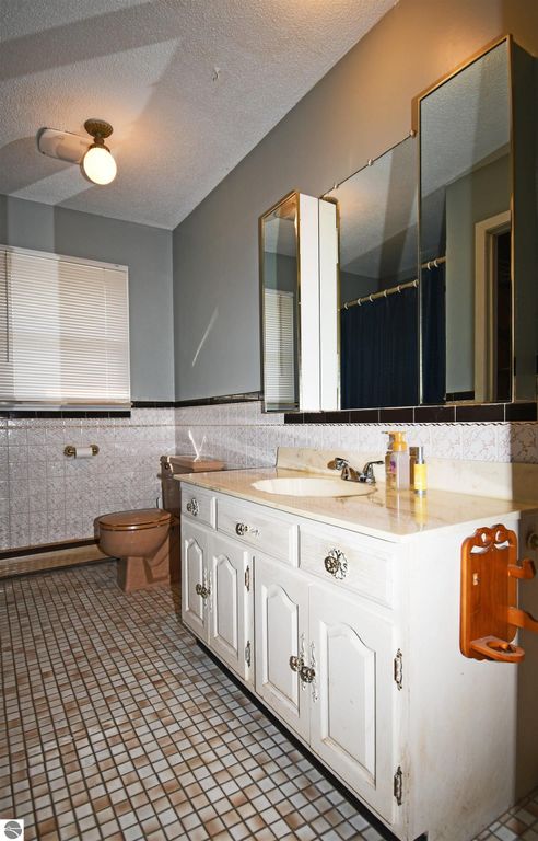 Bathroom interior featuring white cabinetry, dual sinks, large mirror, and tiled floor, with a beige toilet and blue shower curtain, showcasing a clean and functional design in a ranch-style home.