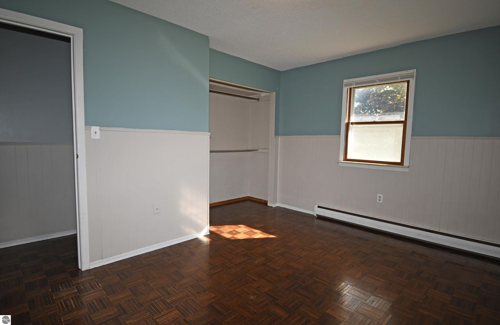 Interior view of a freshly painted 3-bedroom ranch home showcasing a spacious room with parquet flooring, a window allowing natural light, and closet access, highlighting the comfortable living space in Tawas City, MI.