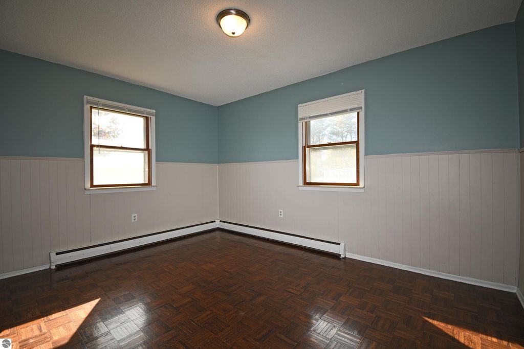 Interior view of a freshly painted bedroom with two windows, light blue walls, and parquet flooring, showcasing the comfortable living space of a ranch home in Tawas City, MI.