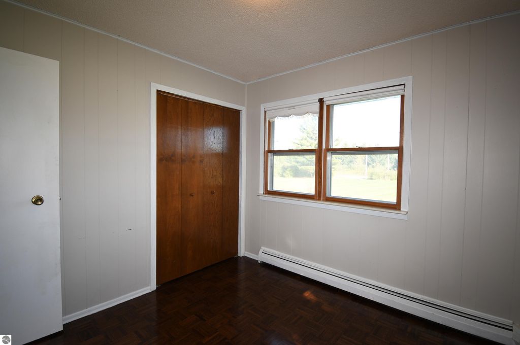 Interior view of a cozy bedroom in a ranch-style home at 2275 Noble Road, featuring wooden closet doors, two windows providing natural light, and light-colored walls, showcasing the comfortable living space on 40 acres in Tawas City, MI.