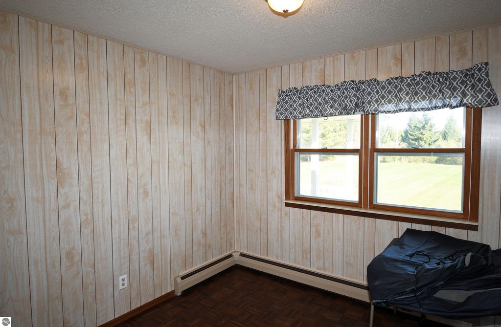 Interior view of a cozy room in a ranch-style home at 2275 Noble Road, featuring wood-paneled walls, two windows with patterned valances, and a corner with a chair, highlighting the comfortable living space on 40 acres in Tawas City, MI.