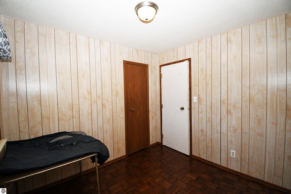 Interior view of a bedroom in a ranch-style home at 2275 Noble Road, featuring wood-paneled walls, a small bed frame, and two doors, highlighting the comfortable living space in a 3-bedroom property on 40 acres in Tawas City.