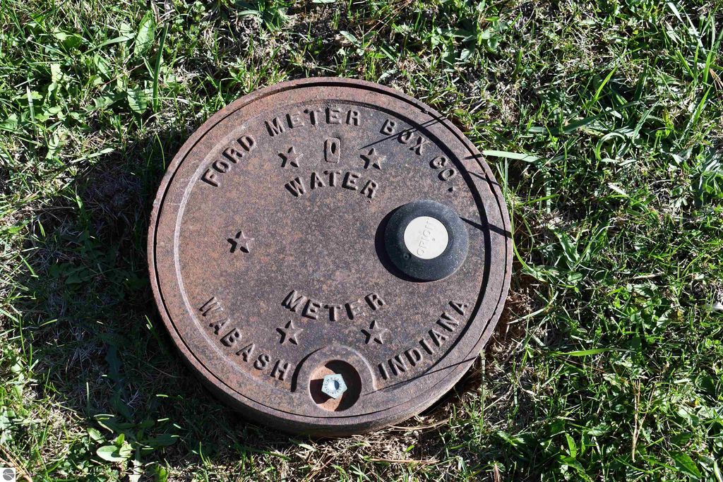 Water meter cover from Ford Meter Box Co., located in Wabash, Indiana, surrounded by grass, indicating city water access for the property at 2275 Noble Road, Tawas City, MI.