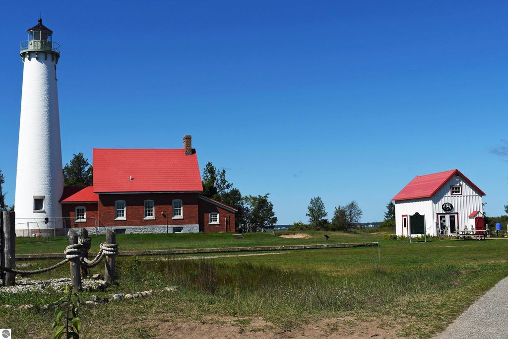 Lighthouse with red-roofed brick building and white cottage in Tawas City, Michigan, surrounded by greenery and blue sky, representing local outdoor lifestyle and proximity to Lake Huron.
