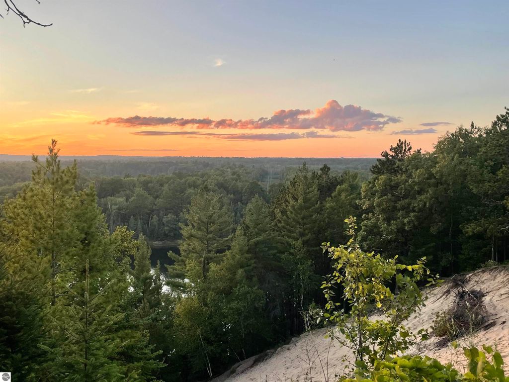 Sunset view over lush green forest and rolling hills near Tawas City, Michigan, highlighting the natural beauty of the 40-acre property for sale.